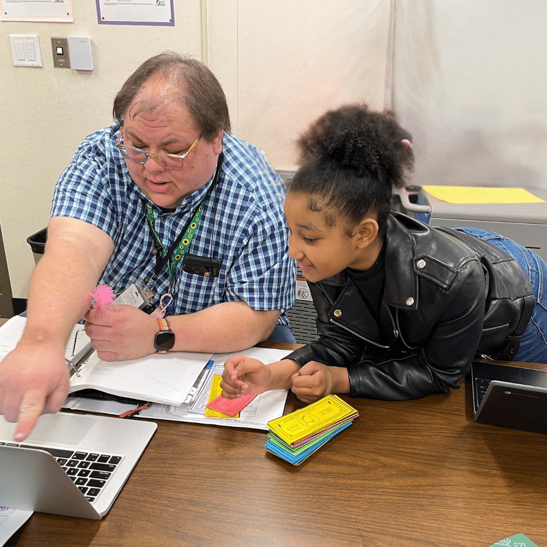 Dalilah, a fourth grade girl, looks at a computer with her mentor while he points at it.